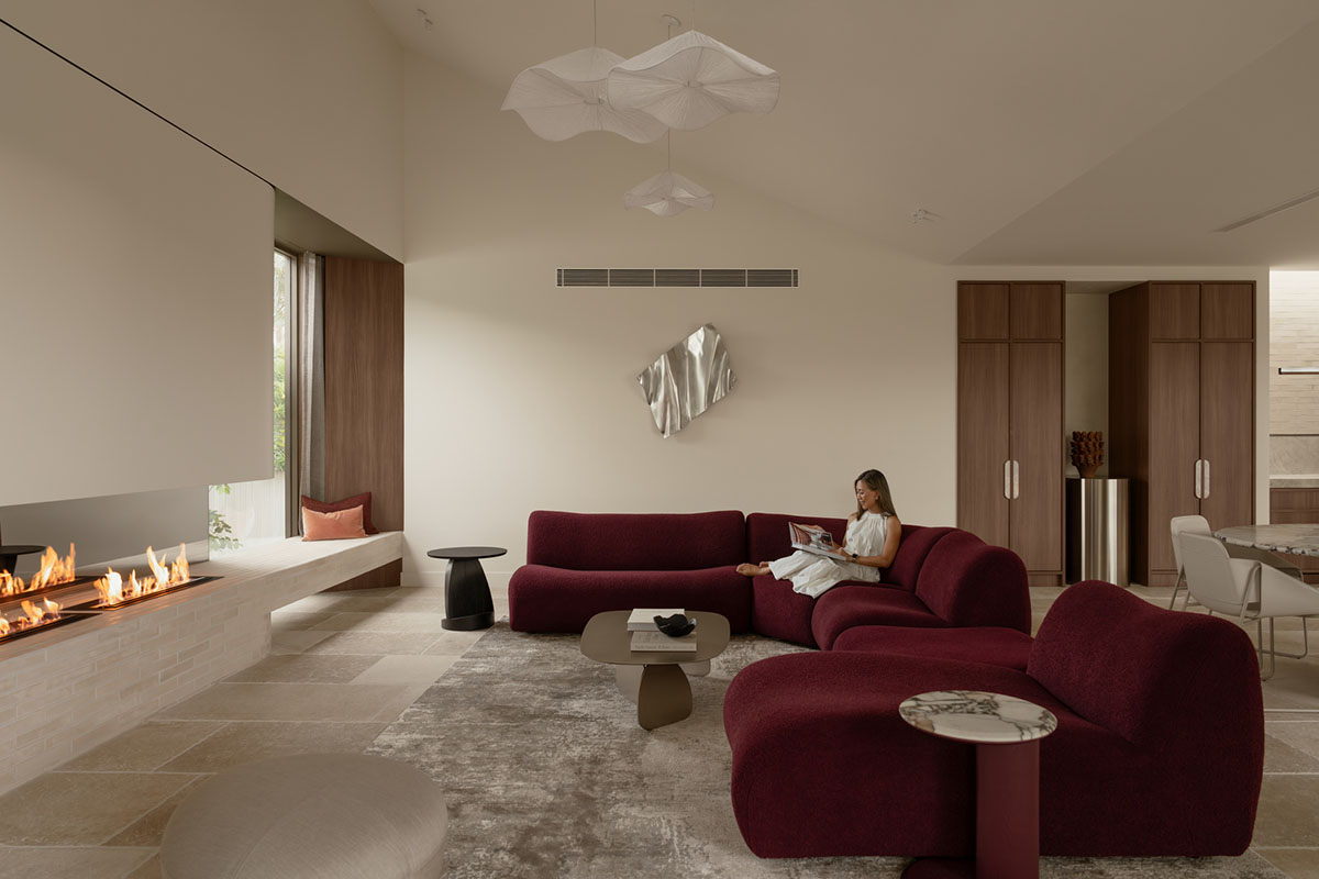Curved modular sofa with chaise in a deep maroon bouclé fabric facing a modern open-style fireplace.