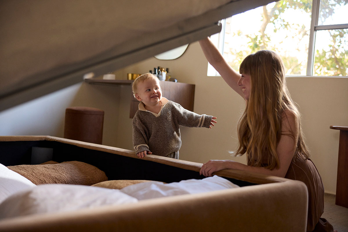 A mother and toddler opening a storage bed in a family home, revealing hidden space for linens.
