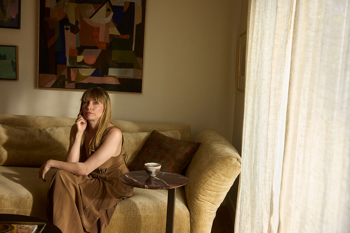 Anna Delprat sat on a modular sofa styled in a warm velvet fabric, captured in her small space, harbourside apartment.