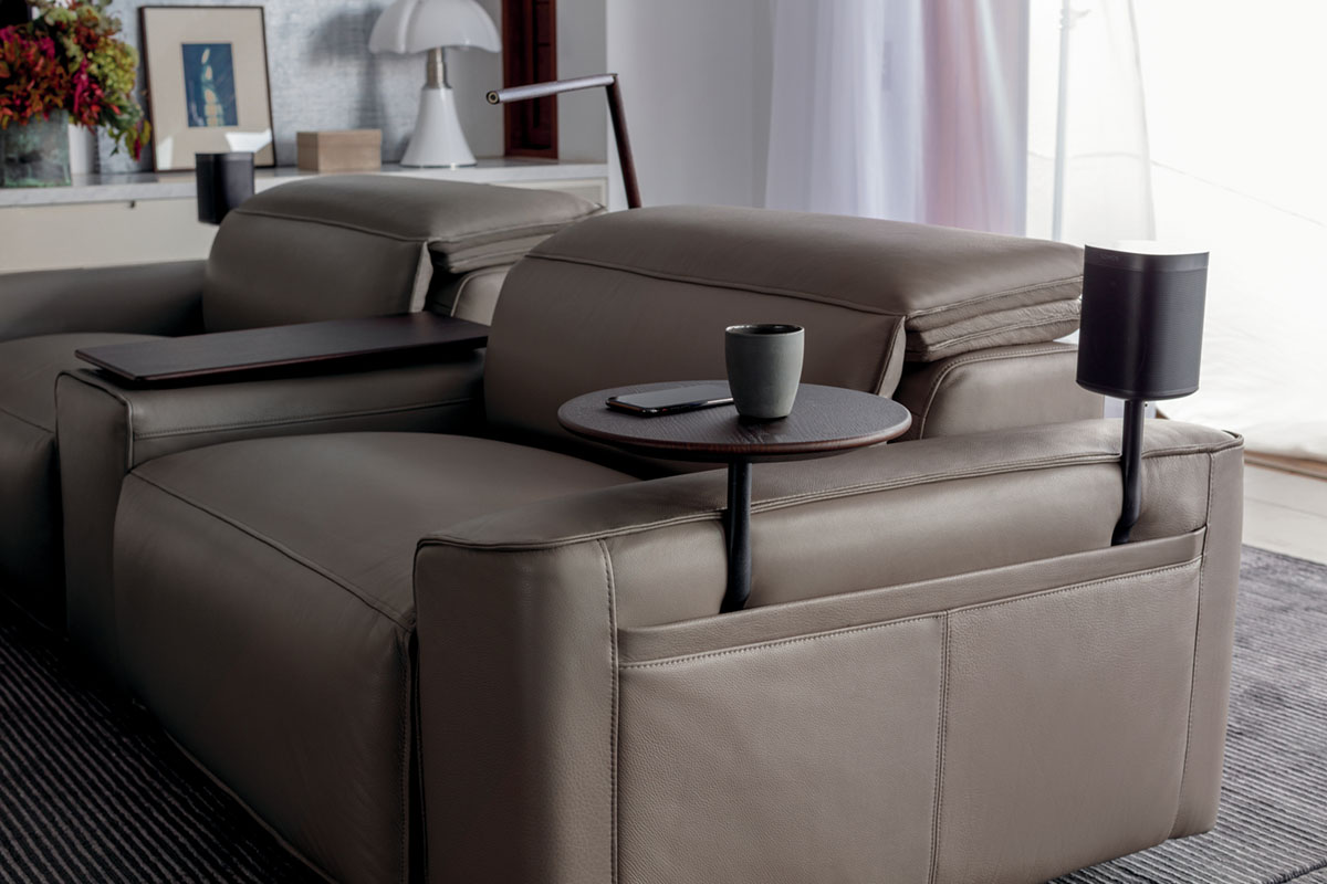 Space-saving recliner sofa in a compact apartment, with integrated smart accessories: charging table, LED light, speaker.