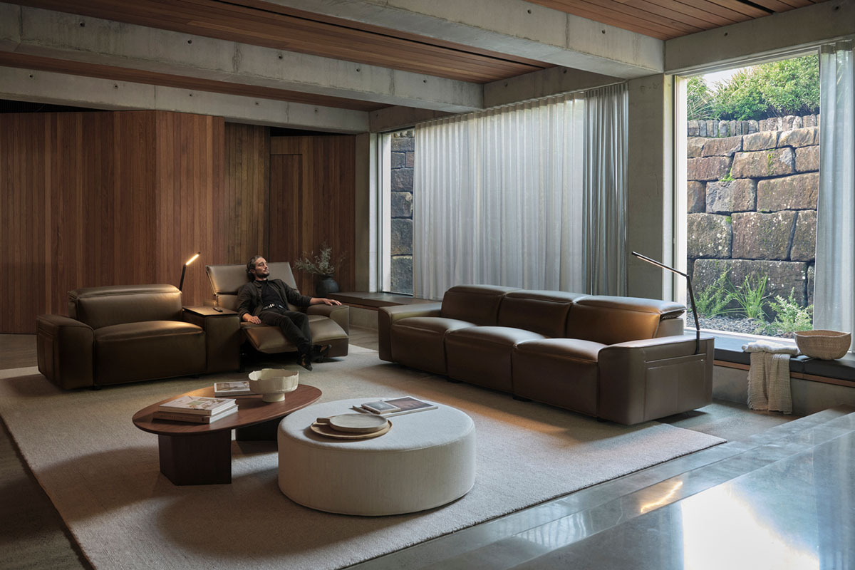 Leather modular recliner and armchair in a timber-lined living room, one seat reclined for a relaxed movie night setup.