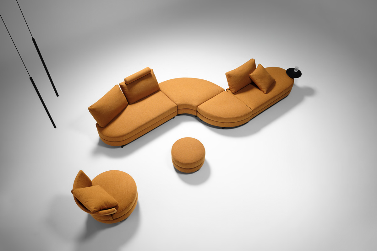 Overhead view of S-shaped curved modular sofa in a warm ochre fabric with matching ottoman and chair.