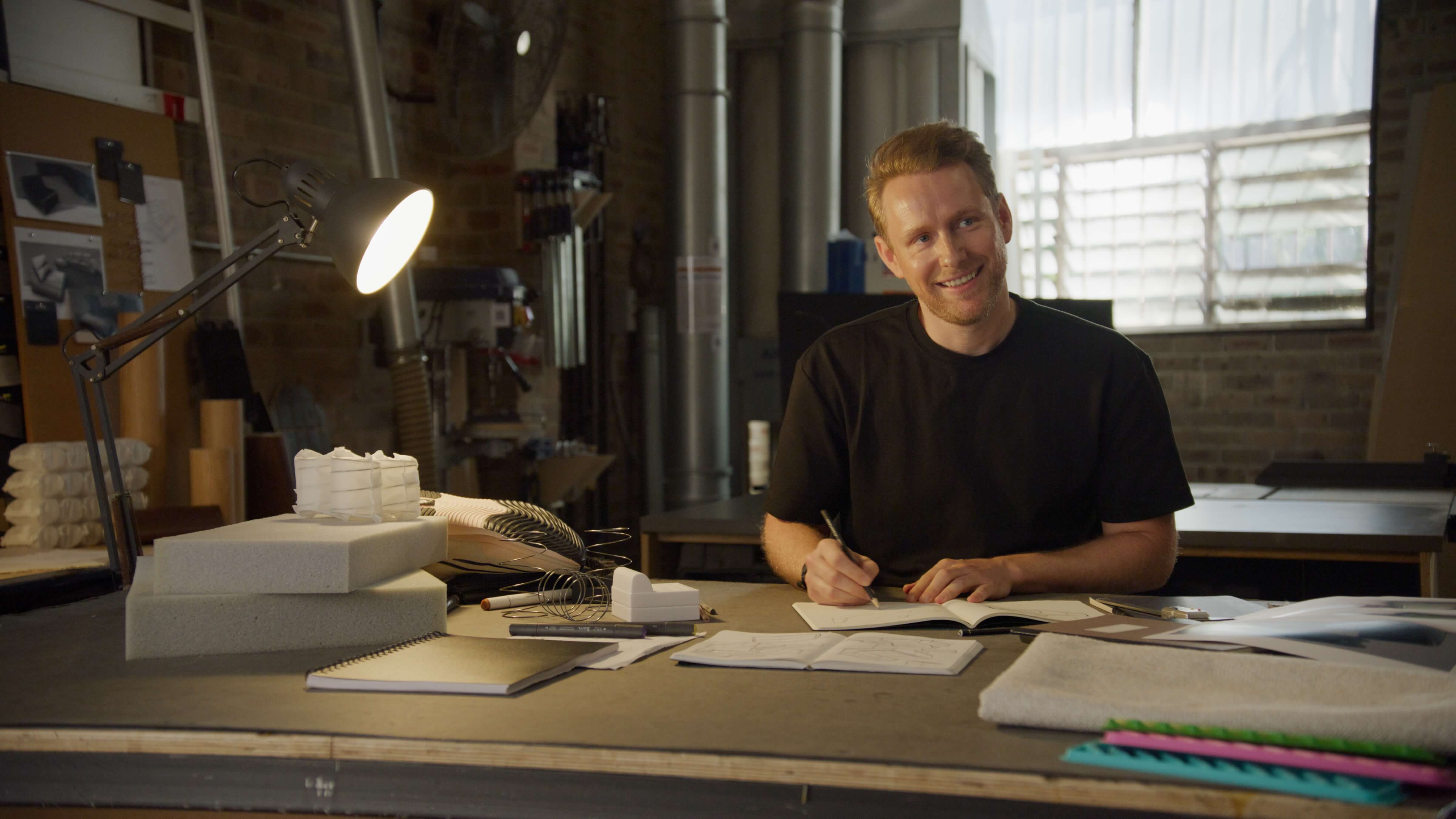Designer sat in workshop smiling, sketching early designs of FreeForm sofas.