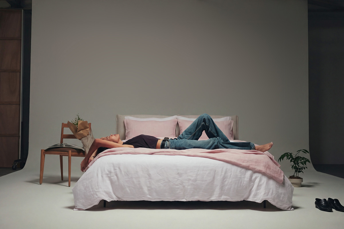Woman lounging comfortably on bed in studio. Styled in light pink and neutral linen bedding.