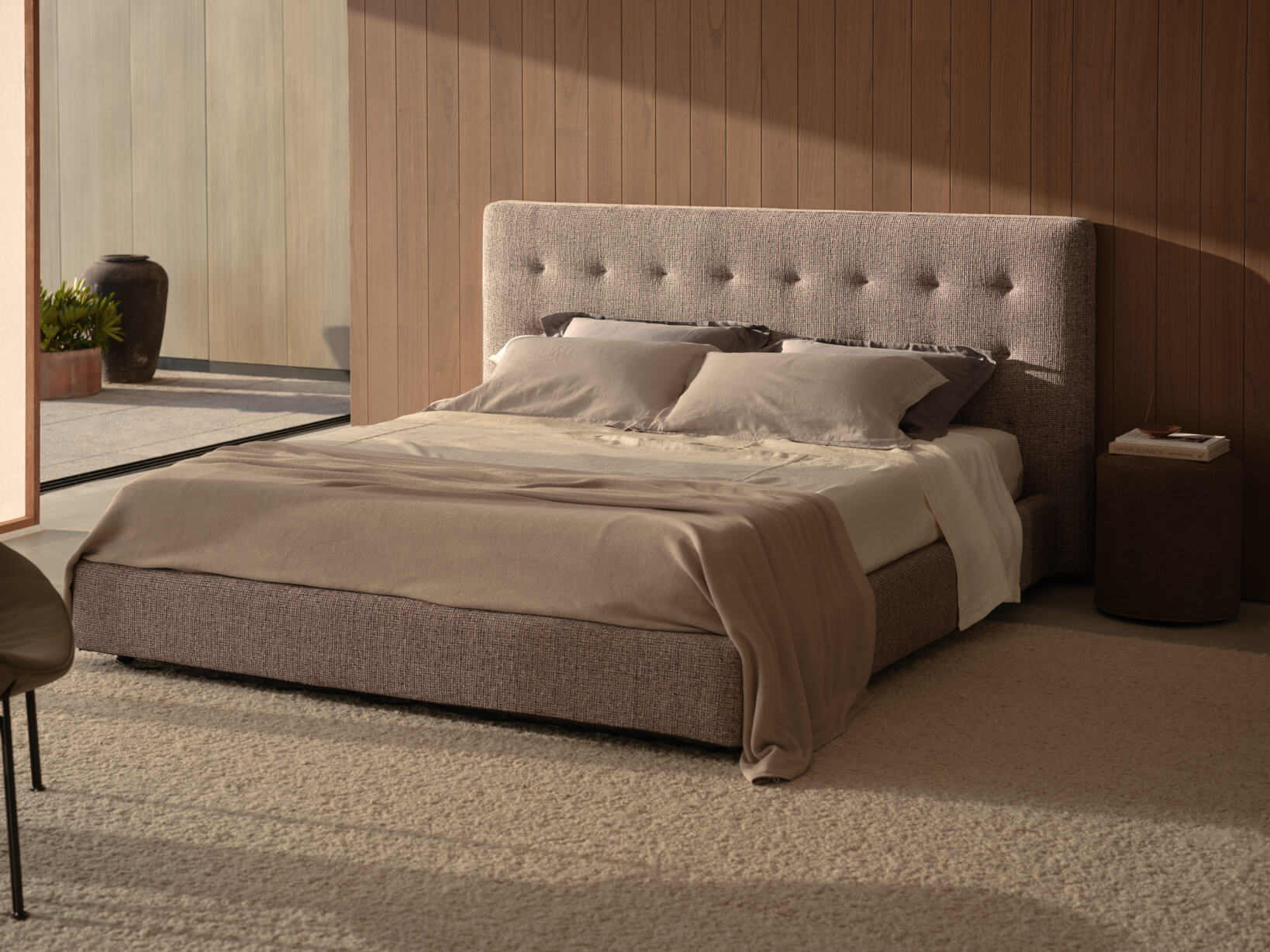 Modern and spacious bedroom with plush pastel bedhead, neutral linens, layered cushions, a sand-toned rug.