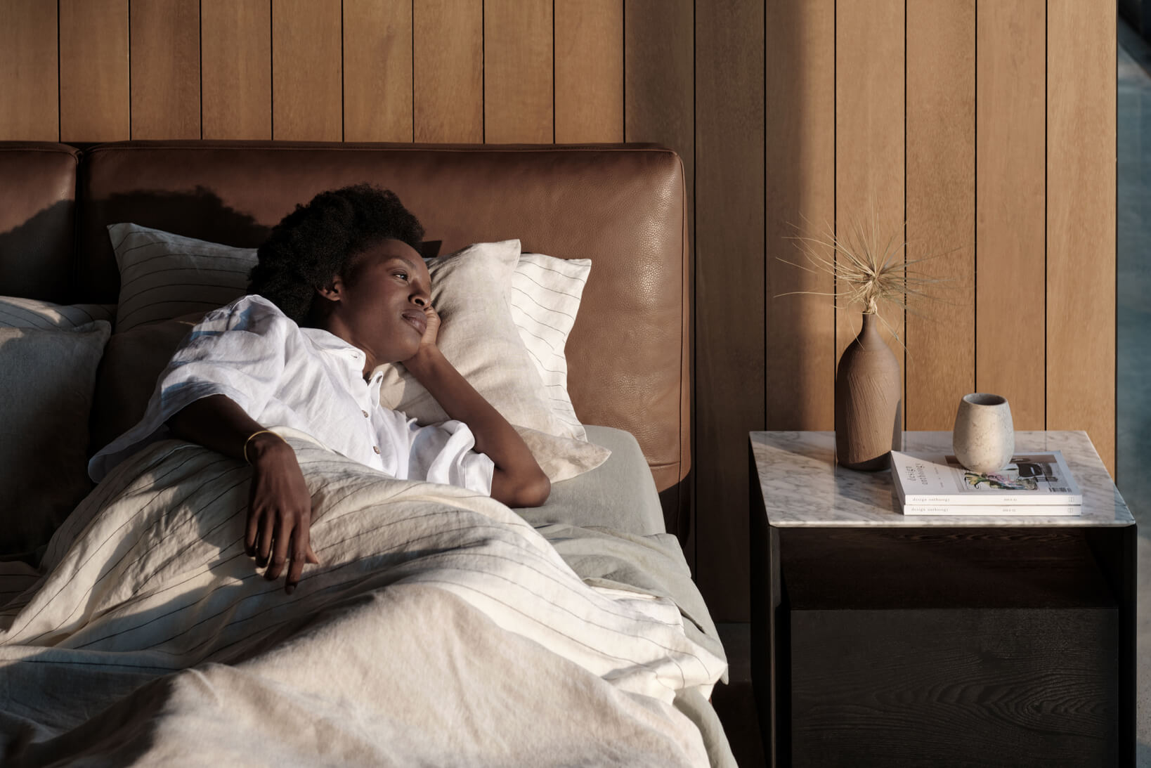 Woman lies on her side on a supportive mattress in a contemporary bed with a brown leather bedhead.