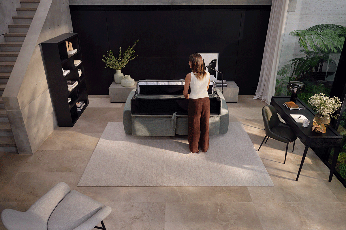 A contemporary living room with a women folding out a light green sofa bed.