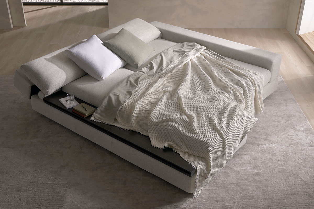 A sofa that has been transformed into a bed with a neutral throw blanket.