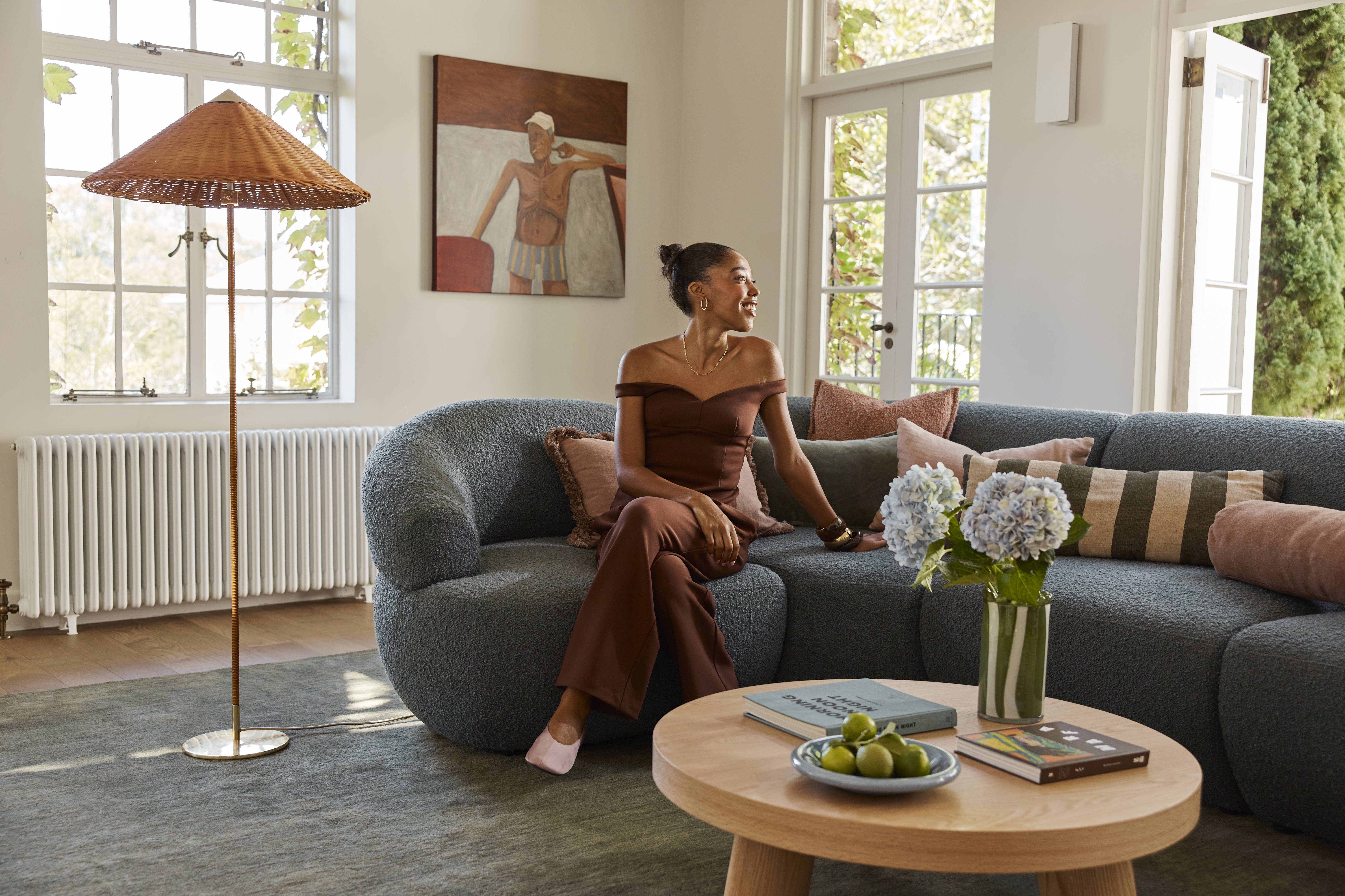 Interior Designer Mariah Burton sits on a teal, bouclé sofa, styled with tactile accents and pops of vibrant pattern and colour. Wall artwork by Dan Rushford. Designer’s own cushions. 