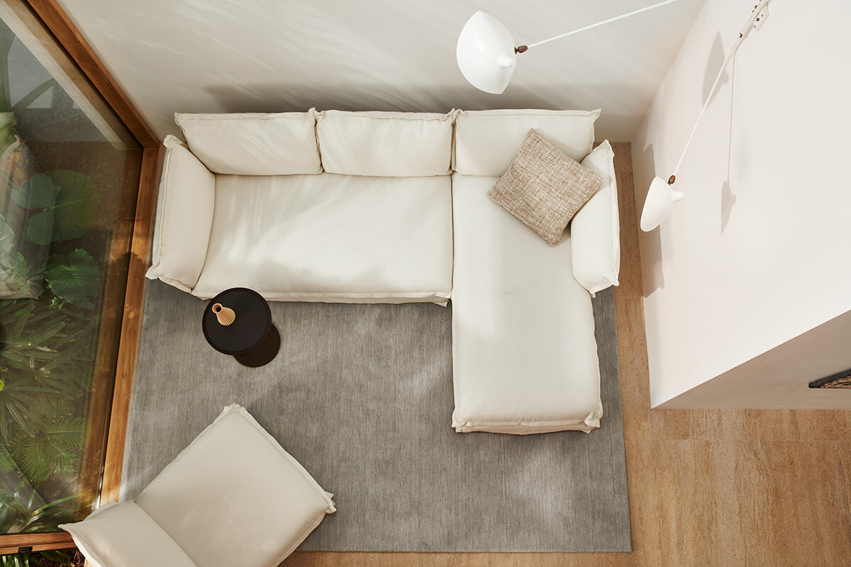 Compact corner sofa with chaise in soft ivory fabric styled with a textured cushion and minimalist black side table, set in a light-filled small space.