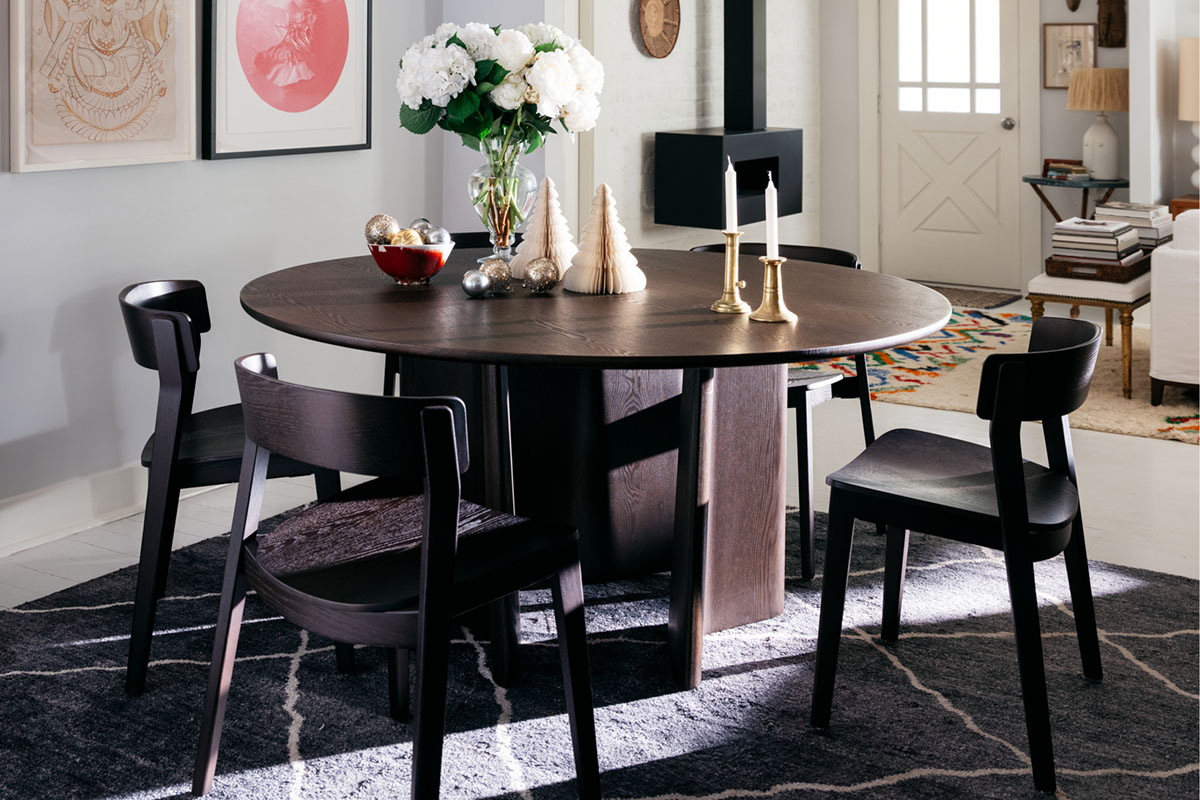 A round dining setting styled for Christmas with white florals, gold candleholders, and elegant tree decorations in a modern interior.