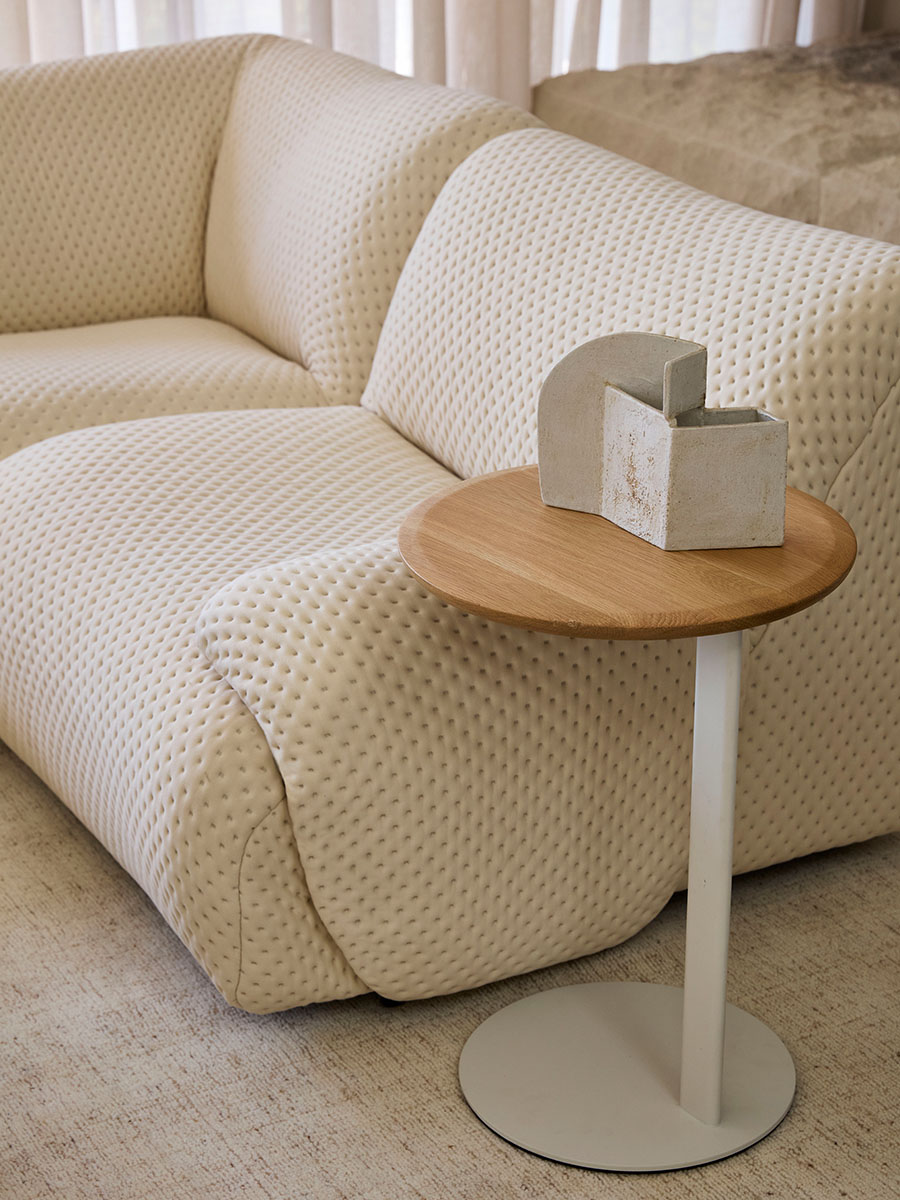 Close-up of a textured neutral sofa beside a round side table featuring sculptural objects.