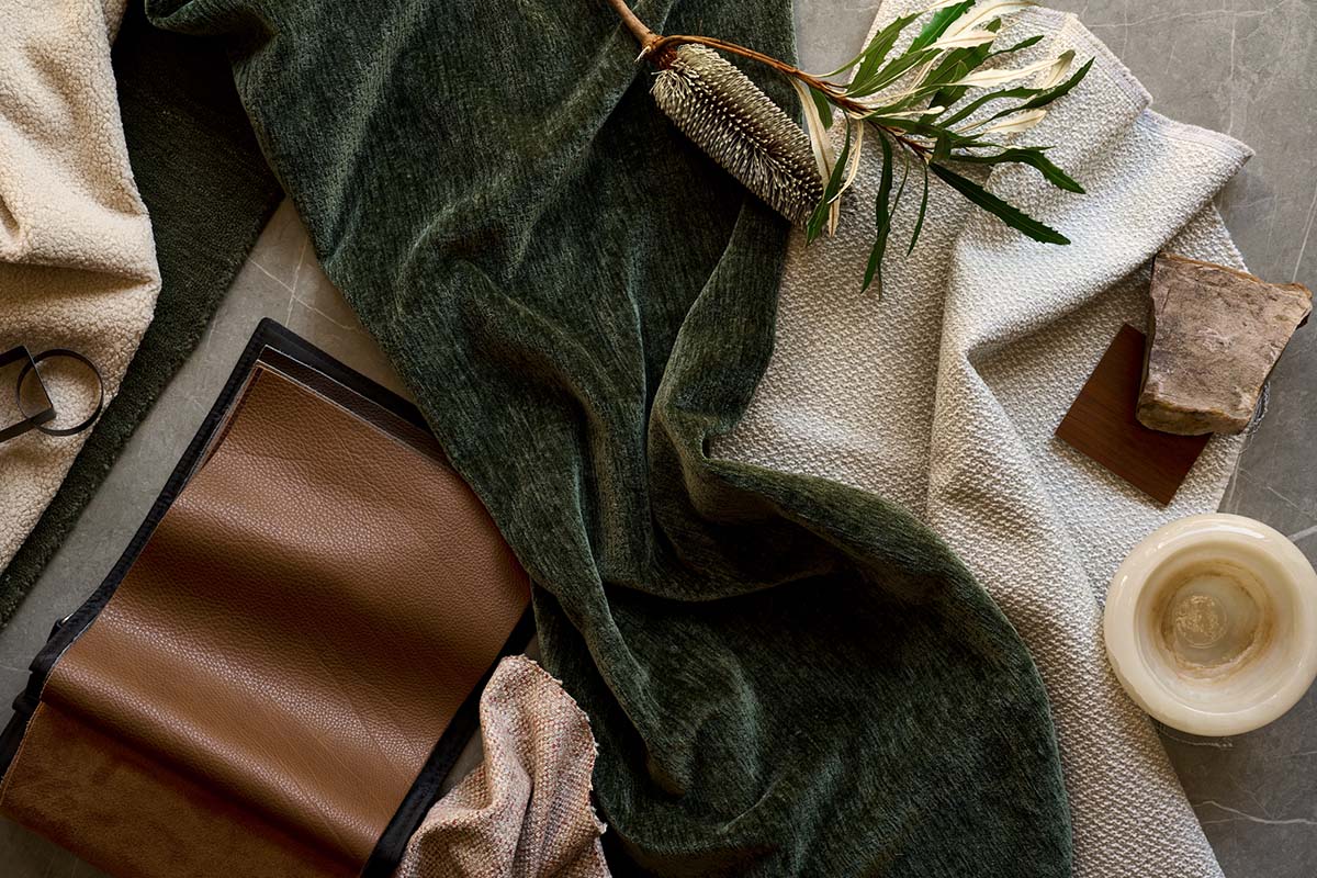 Fabric swatches in cream, green and brown arranged with leather sample, stone and foliage.