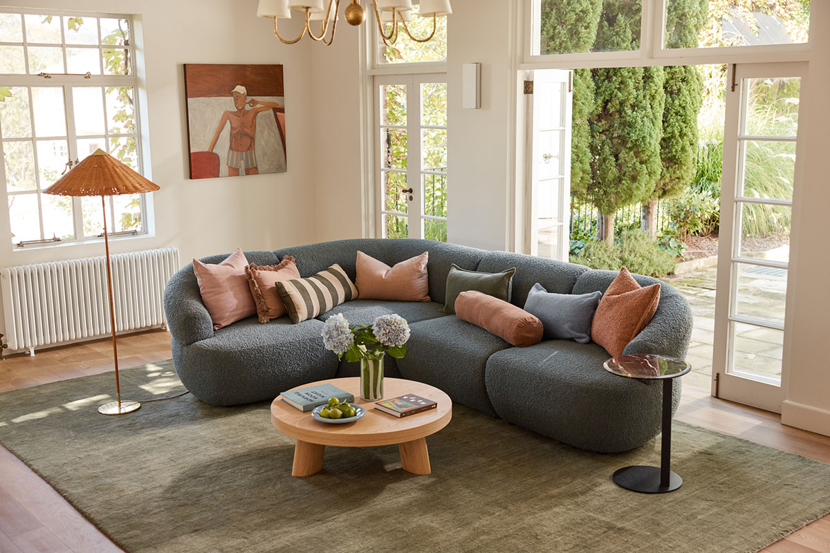 A modular blue bouclé sofa styled with blush and fern accents in a light-filled contemporary living room.